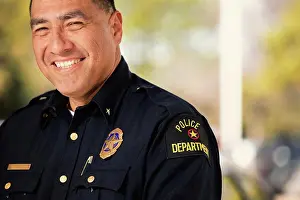 First Responders Prints: Portrait of Police officer standing outside with arms crossed looking towards camera smiling