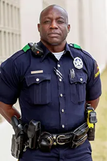 Bald Prints: Portrait of Police officer Standing in street in front of squad car looking towards camera with arms behind his back