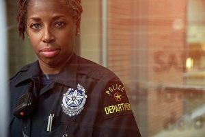 Lighthearted Prints: Portrait of Police woman standing in front of large glass window with reflections looking towards camera