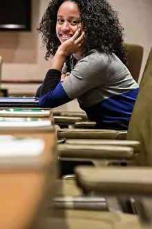 Point Of View Prints: A portrait of a smiling black businesswoman sitting at a conference table turning her head and looking at the camera