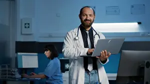 Assistant Prints: Portrait of smiling doctor wearing medical coat and stethoscope holding laptop computer