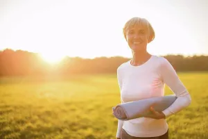 Best Prints: Portrait of smiling senior woman holding yoga mat on rural meadow at sunset