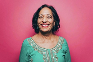 Asian And Indian Ethnicities Prints: Portrait of smiling senior woman wearing salwar kameez against pink background
