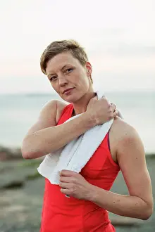 Vertically Prints: Portrait of sporty woman wiping sweat with towel outdoors