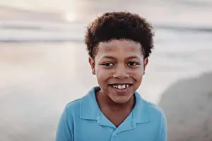 Forehead Prints: Portrait of young school-aged boy smiling at beach during sunset