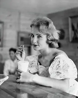 Beverage Prints: Portrait of a young woman drinking a milkshake at a bar counter