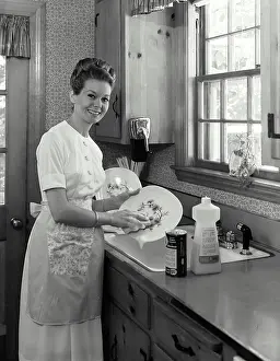 Apron Prints: Portrait of young woman washing dishes in kitchen