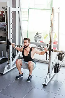 Heavy Prints: Powerful determined sportsman doing exercise with barbell at squat rack during weightlifting training with personal