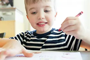 Thoughtful Prints: Preschool Age Boy Holds Red Crayon in Hand While Drawing