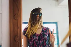 Refle Ction Prints: Pretty woman standing at mirror with sunglasses over hair and gesturing two fingers