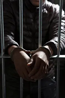 Justice Prints: A prisoner behind bars with hands cuffed