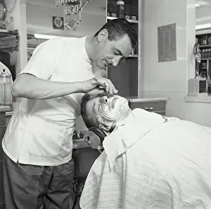45 50 Years Prints: Side profile of a barber shaving a mid adult man in a barbershop
