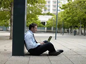 Business Person Prints: Side profile of businessman sitting at roadside and using laptop