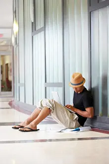 Corridor Prints: Side profile of a college student sitting in a corridor and using a laptop