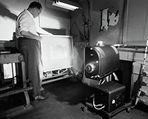 Rolled Up Sleeves Prints: Side profile of a male worker operating a photoengraving camera
