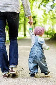 Verticals Prints: Rear view of baby girl holding mother's hand while walking on dirt road