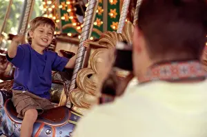4 5 Years Prints: Rear view of a father taking a photograph of his son riding a carousel horse