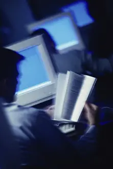 Instruction Prints: Rear view of a man reading a book in front of a computer monitor