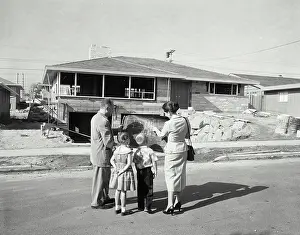 Beginnings Prints: Rear view of a mature couple and their children standing in front of a house and looking at a blueprint