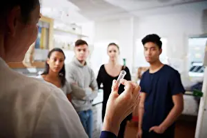 Instruction Prints: Rear view of mature female teacher holding test tube explaining to young multi-ethnic students in laboratory