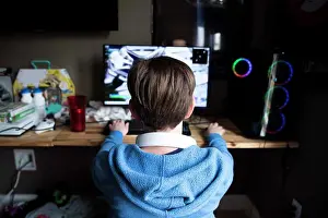 Electronics Prints: Rear View of Teen Boy Playing Gaming Computer on a Messy Desk