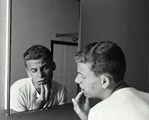 Jul06 Prints: Rear view of a teenage boy looking at a mirror with his hand on his chin, 1960