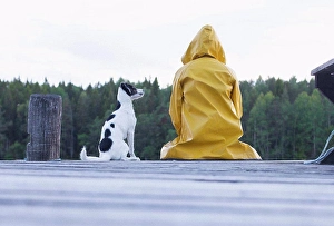 Pet Owner Prints: Rear view of woman wearing yellow raincoat sitting with dog on jetty at forest