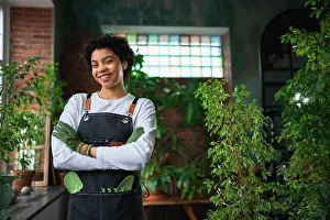 Arbeiten Prints: Running of own business. African woman florist wearing apron in botanical store with green plants