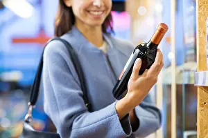 Purchase Prints: sale, shopping, consumerism and people concept - happy young woman choosing and buying wine in market or liquor store