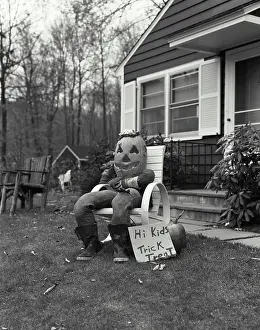 Humor Prints: Scarecrow in a Halloween costume sitting in an armchair in front of a house