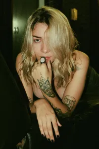 Voluptuous Prints: Seductive inviting fair haired tattooed woman in black bra and jeans sitting on sofa with legs spread wide