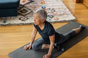 Asian And Indian Ethnicities Prints: Senior asian woman stretching on exercise mat in living room