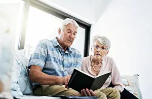 Paperwork Prints: Senior couple, living room and reading on notebook in sofa at home with shopping list for household