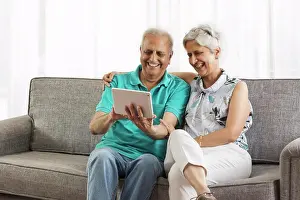 Arms Around Prints: Senior couple sitting on sofa using digital tablet