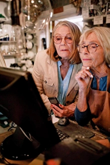 Business And Occupation Prints: Senior female customer and saleswoman looking at computer monitor in hardware store
