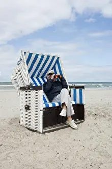 Three Quarter Front View Prints: A senior man sitting in a hooded beach chair looking through binoculars