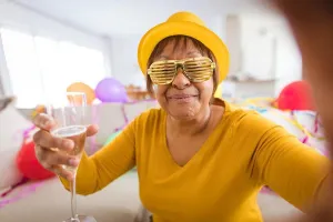 Video Prints: Senior woman in shutter glasses making video call while enjoying champagne during party at home