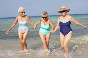 Senior women walking in waves on beach