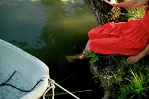 Calm Prints: Serene moment as a woman in a bright red dress dips her feet in the water beside a moored boat