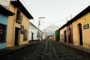 Colonial Architecture Prints: A serene morning in a colorful, cobblestone street with a volcano looming in the distance