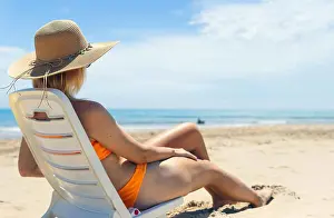 Outstretched Prints: sexy tanned girl is sitting on a sun lounger in an orange swimsuit and a brown hat
