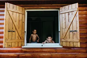 Timber Prints: Two shirtless African American brothers looking out open window of wooden house while having fun at home together