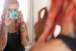 Assured Prints: Over shoulder mirror view of young woman with pink dreadlocks taking selfie