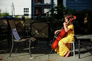 Focused Prints: Side-view of focused, barefoot girl playing cello outside in costume