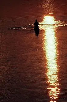 Verticals Prints: Silhouette of a man rowing a boat amidst the river