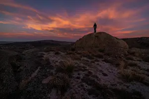 Silhouette of unrecognizable explorer standing on boulder against cloudy sundown sky during trip in mountainous terrain