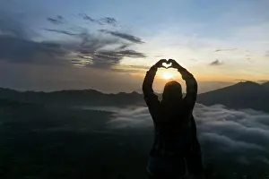 Overlooking Prints: Silhouette of a young woman fingers forming a heart at dawn, Uluwatu, Bali, Indonesia