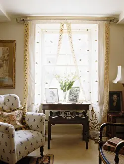 Tables Prints: Small cream patterned armchair beside window with patterned cream voile curtains