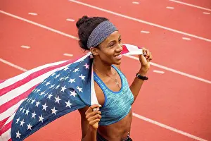 Gleeful Prints: Smiling Black athlete holding American flag on track