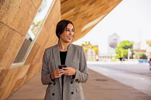 20 To 25 Years Prints: Smiling businesswoman holding smart phone on footpath